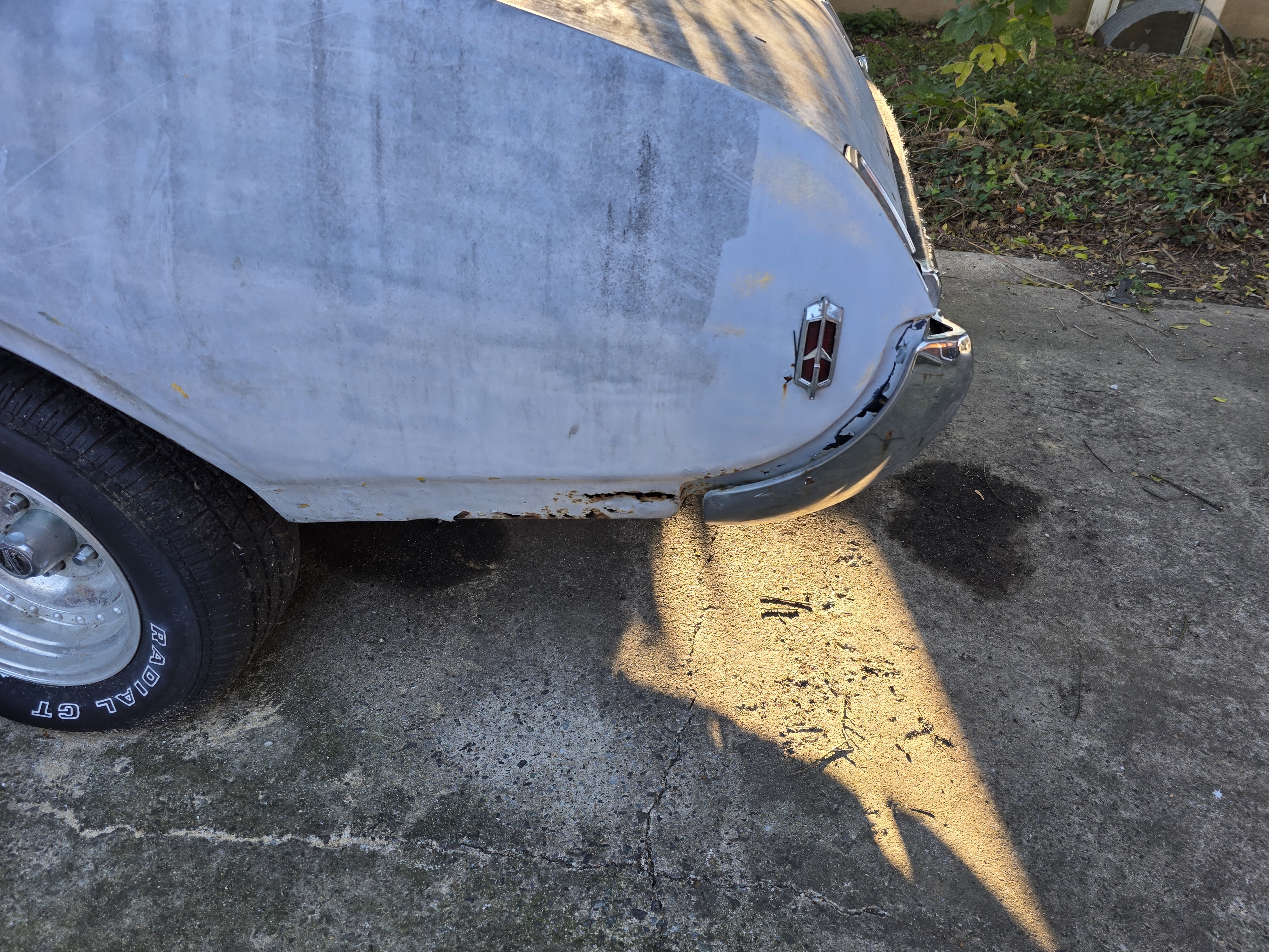 Rust through at the passenger rear quarter and bumper filler junction on a 1969 Cutlass S, original Oldsmobile rocket badge still mounted above. Caption: The patch goes below. The rocket stays.