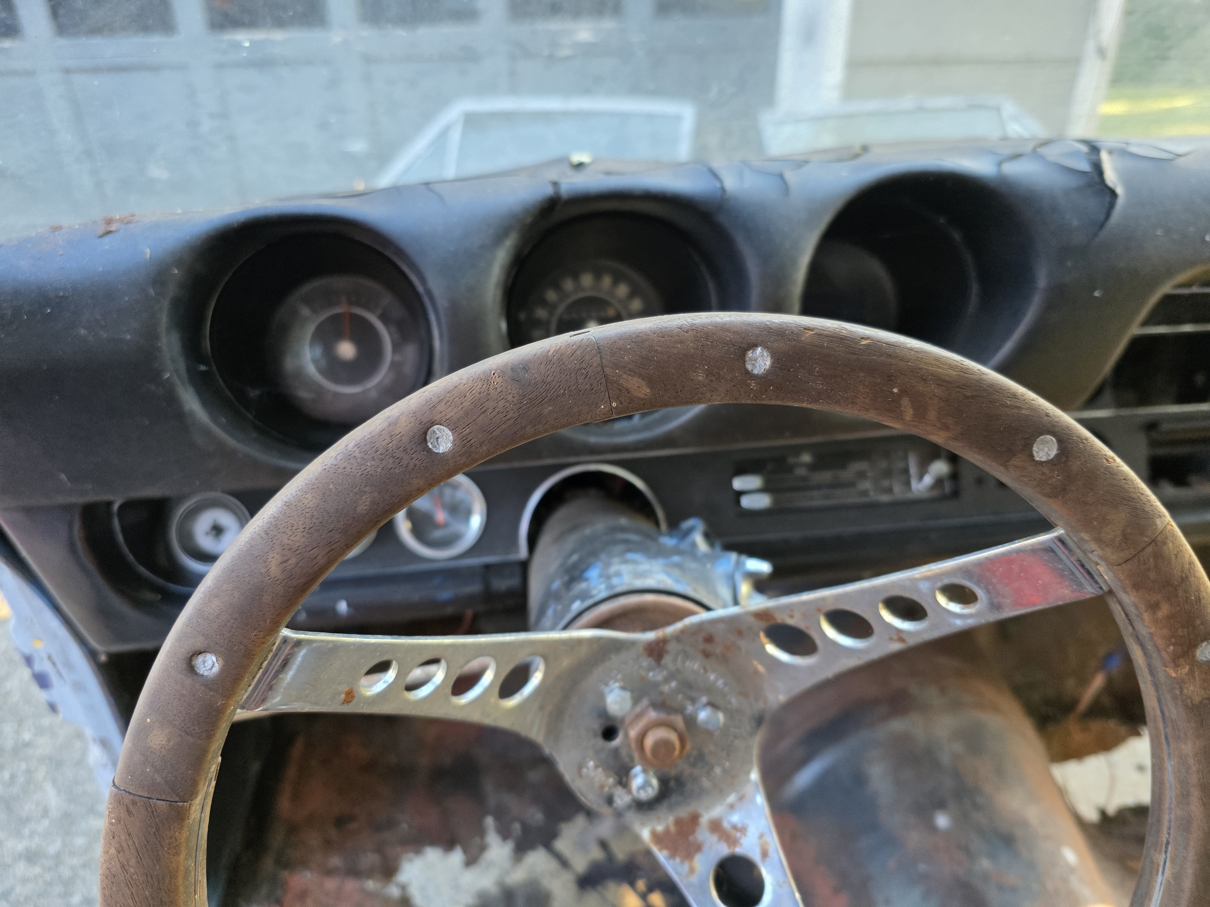 Vintage wood rim steering wheel with drilled chrome spokes in front of the original 1969 Cutlass gauge cluster.